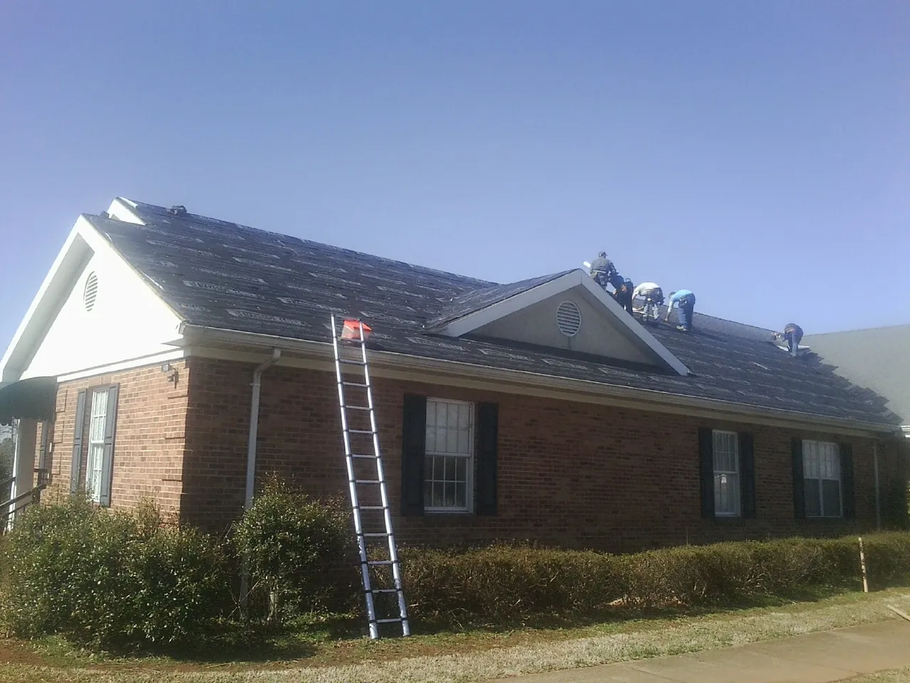 Crew tearing shingles off a brick ranch roof with a ladder set — Metal Roof Repair work by our crew in Scottsburg