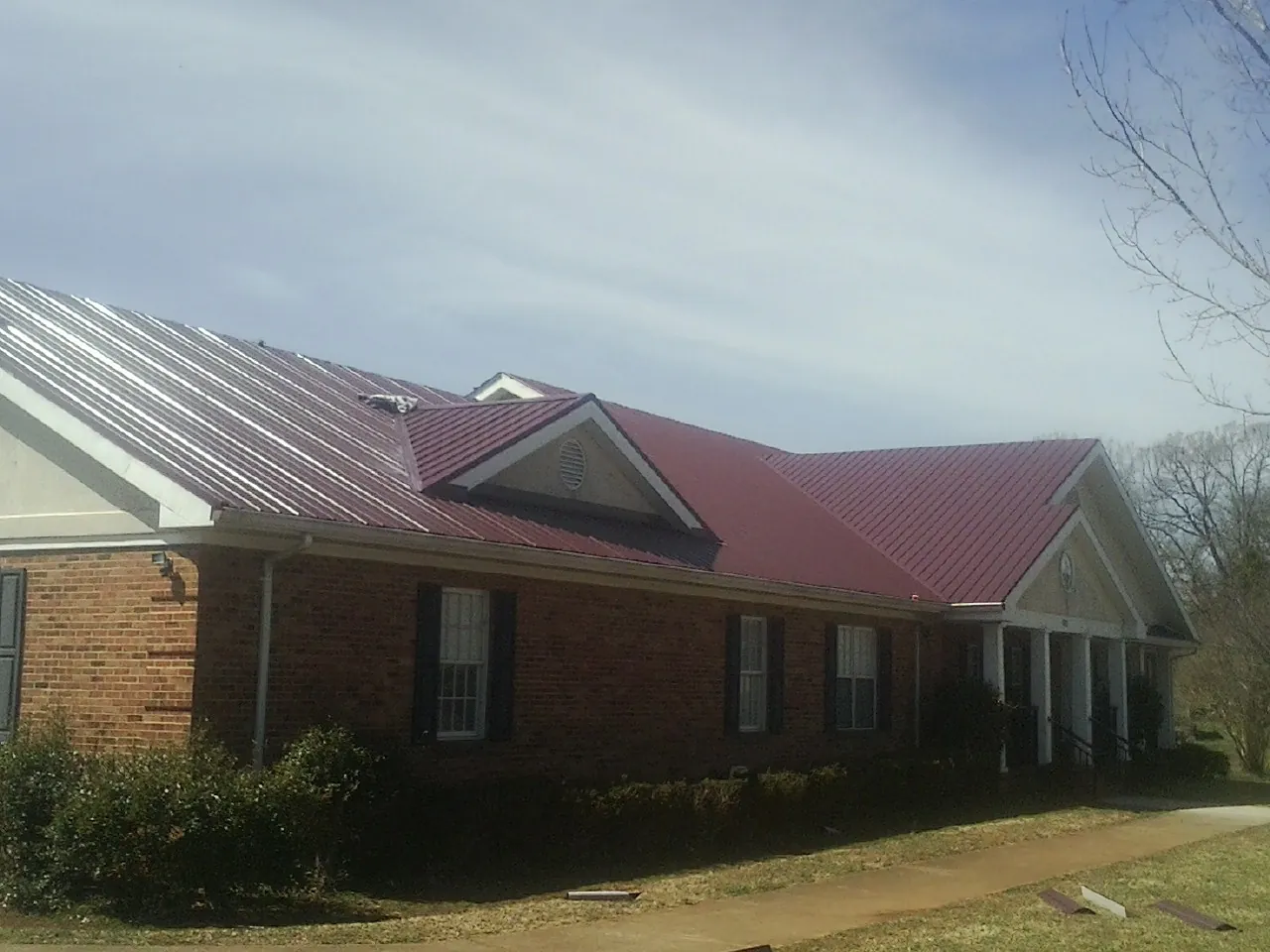 Red metal roof with gabled entries on a long brick building, from a Hail Damage Roof Repair job in Scottsburg